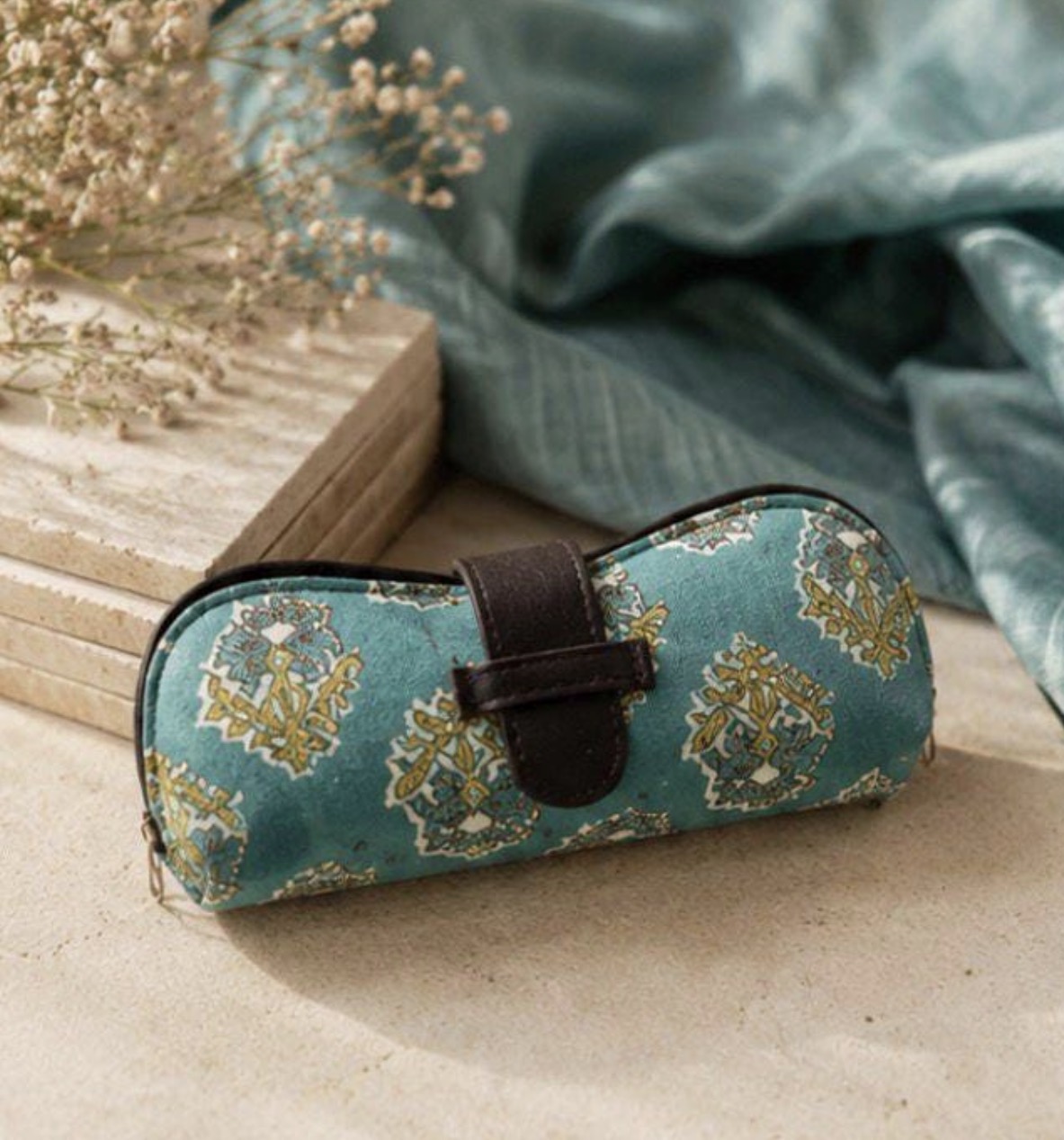 Teal hand block-print Varnya glasses case with leather strap closure on a silk backdrop