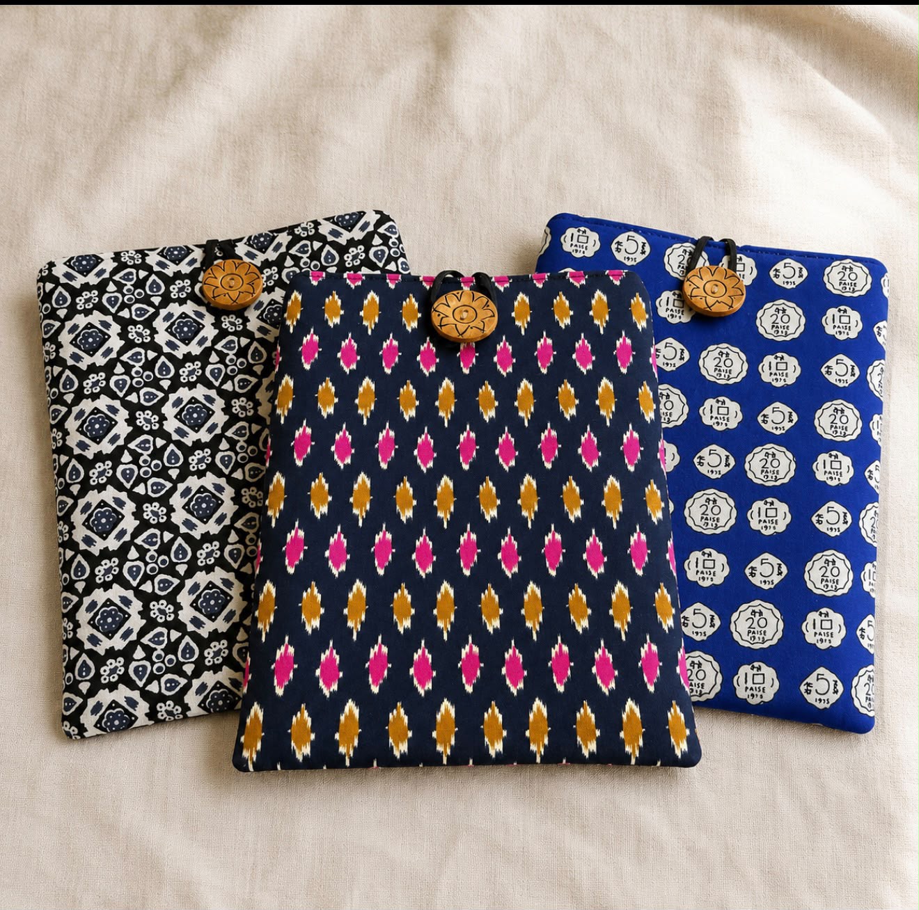 Three padded Varnya book sleeves in indigo, ikat and coin block prints with wooden button closures