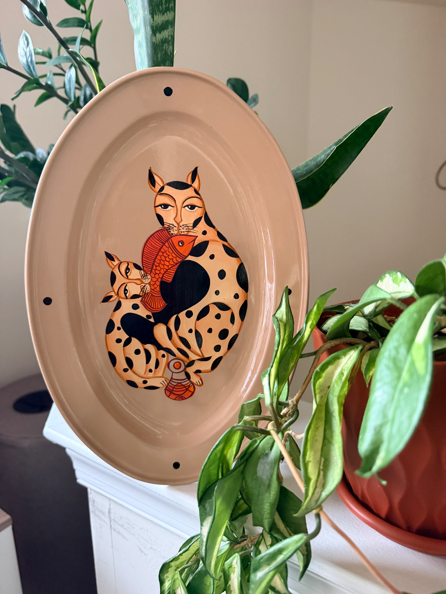 Kalighat Cat Family steel tray standing upright among houseplants
