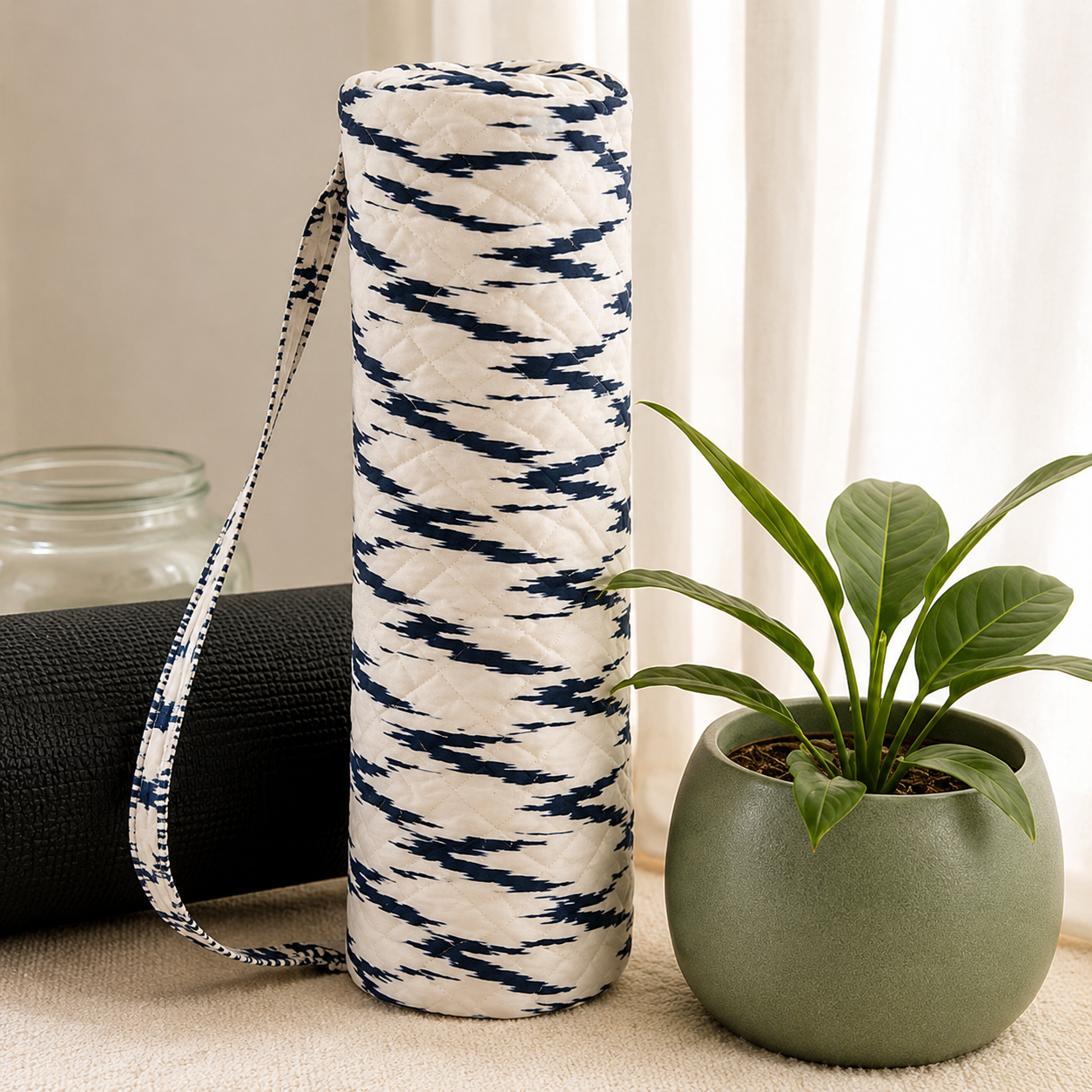 Indigo ikat hand-quilted Varnya yoga mat bag beside a rolled mat and a potted plant